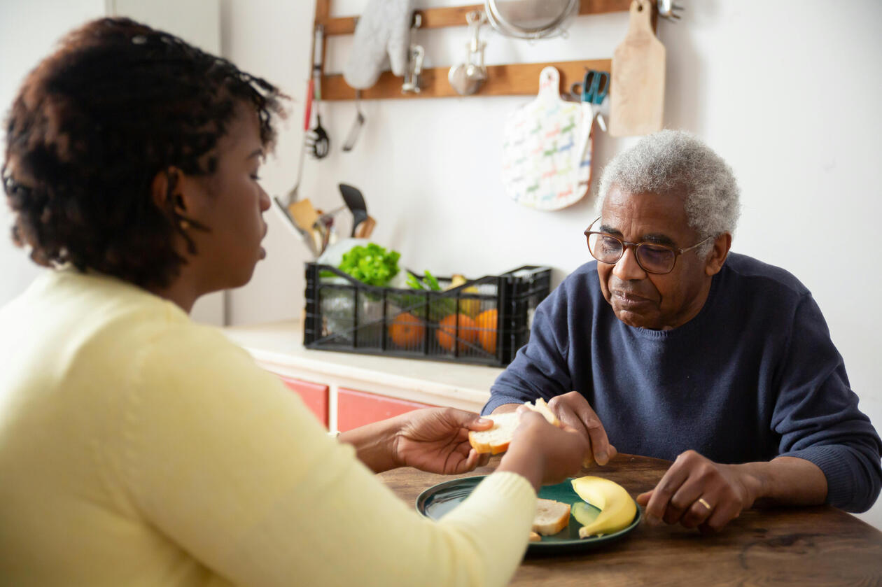 A picture of an elderly man and his female care giver feeding him.